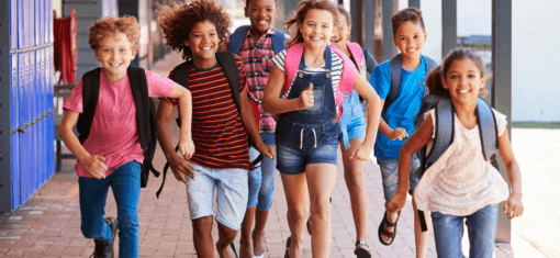 Children with backpacks walking together outside a school building.