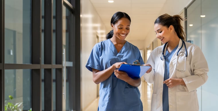Two doctors walking down hallway looking at clipboard