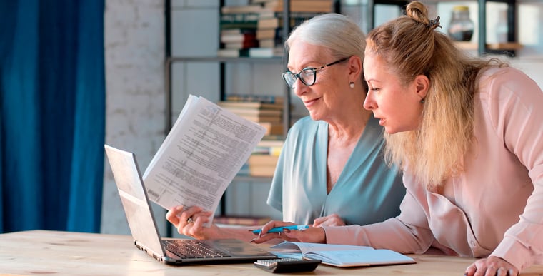 Two woman looking through papers and laptop together