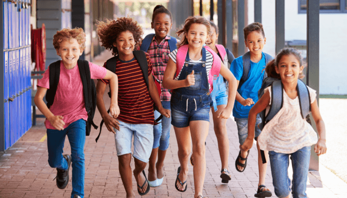 Children with backpacks walking together outside a school building.