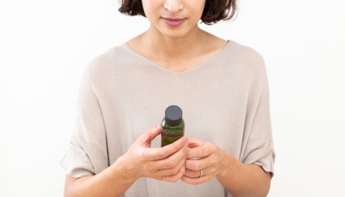 A woman holds a skincare product bottle, considering a purchase.