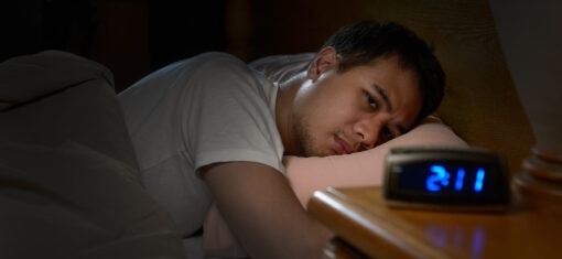A man is lying in bed with eyes wide open, unable to sleep; in the foreground, a digital clock reads 2:00.