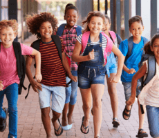 Children with backpacks walking together outside a school building.