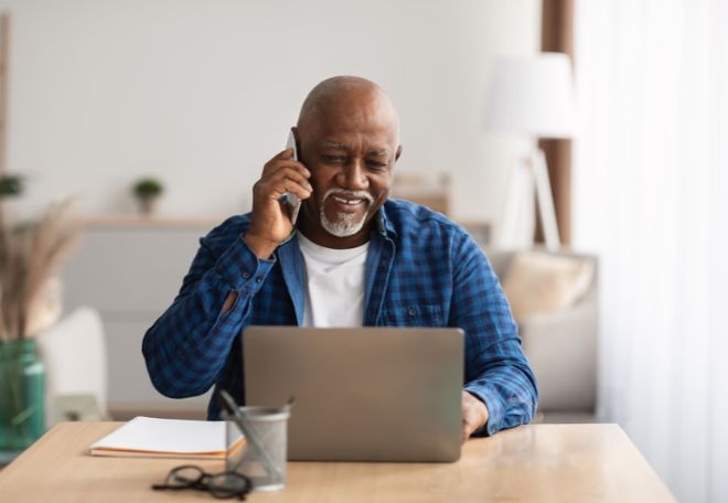 a man talks on a mobile phone while looking at a computer