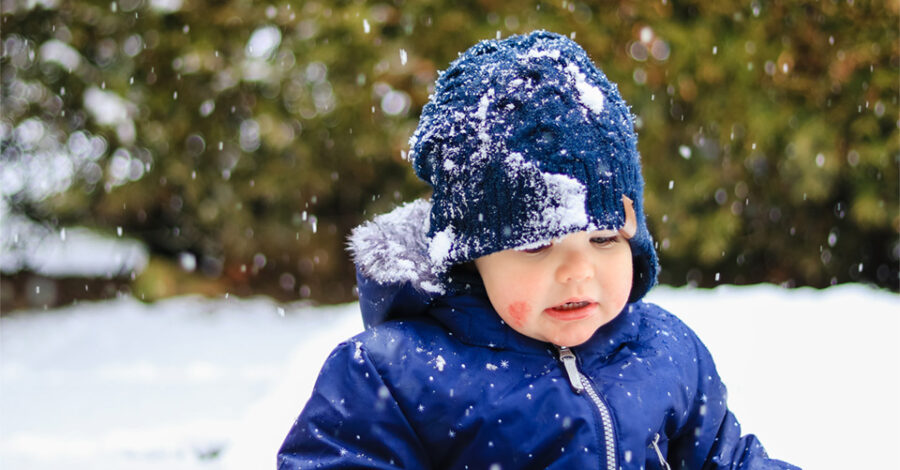 Toddler with eczema is playing in the snow in a winter coat and hat