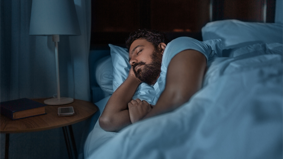 A bearded man is sleeping peacefully in bed in a dark bedroom