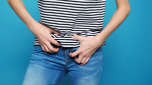 woman scratching crotch through jeans on blue background