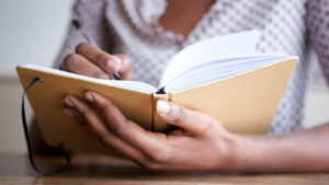 Close up of woman’s hands holding and writing in a yellow journal