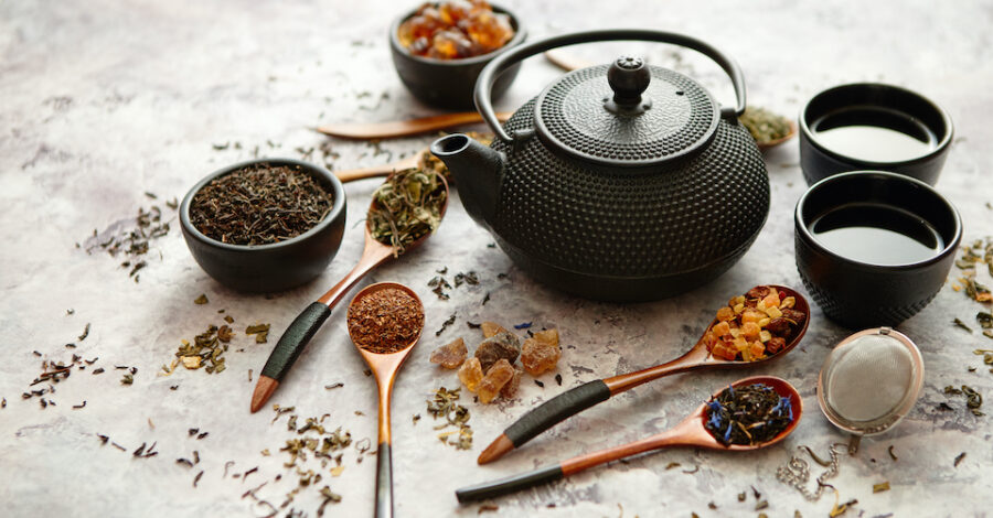 Iron vintage teapot and cups. Dried various kinds of tea on wooden spoons. Stone background with copy space