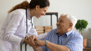 A doctor is leaning over from a standing position to connect with her elderly patient. Both are smiling and gratified.