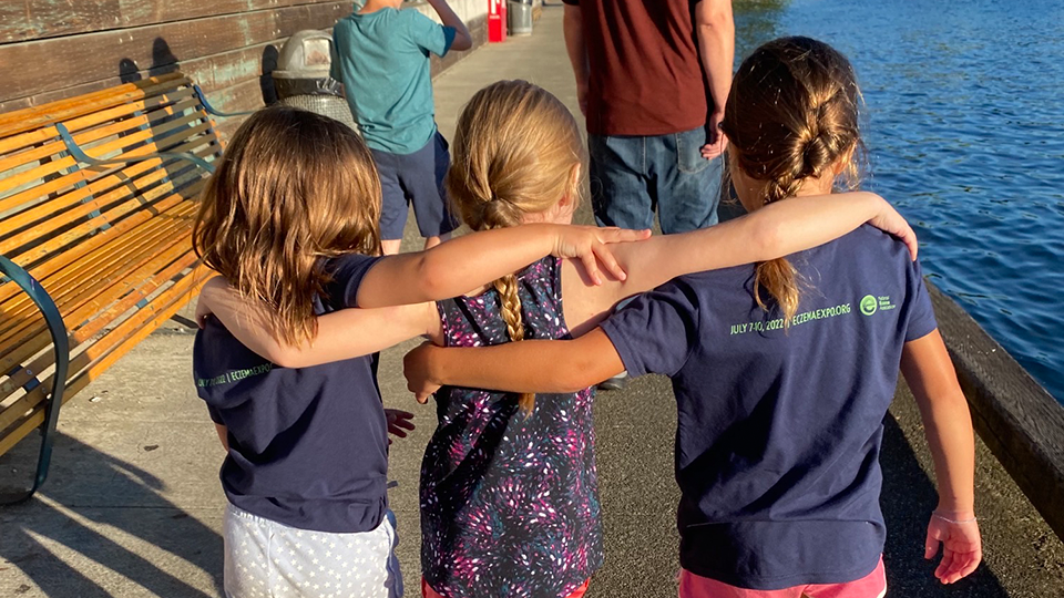 Ella Crnelich and her two sisters are walking away from the camera with their arms around each other’s shoulders.