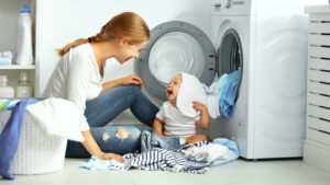 mother with a baby engaged in laundry fold clothes into the washing machine