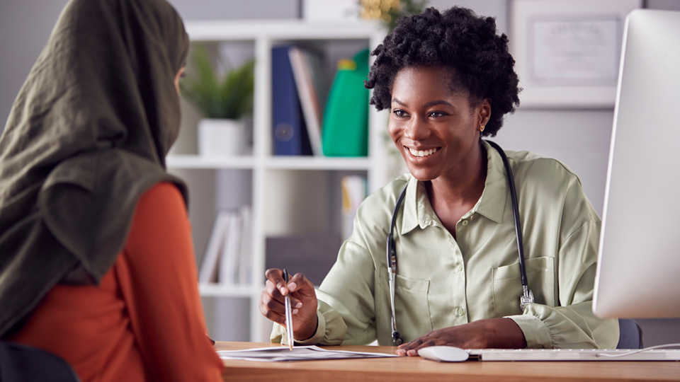 Black woman healthcare professional helps another woman with her back to the camera in a cozy office space with bookshelves