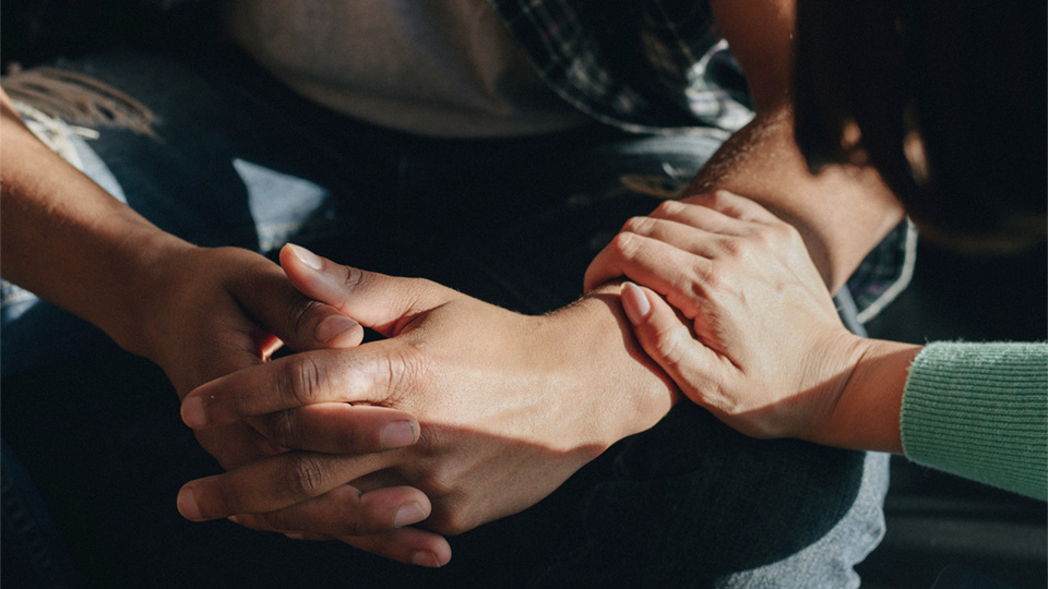 Close-up of two people's hands, a woman has her hand on a man's forearm to show comfort