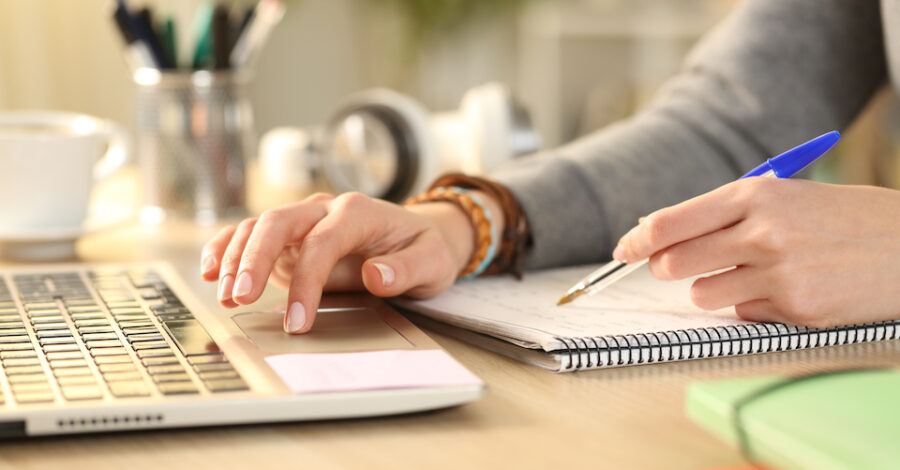 Person's hands comparing notes against a laptop on a desk