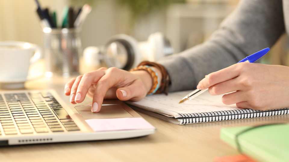 Person's hands comparing notes against a laptop on a desk