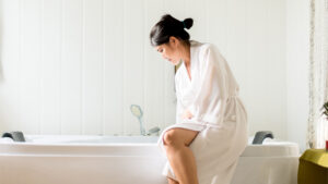 woman sits on edge of bath as she fills it up with water and bleach