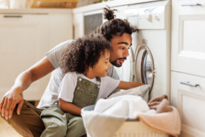 Cheerful kid boy sitting on dad's lap and helping with laundry